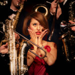 press photo of Raye surrounded by saxophones and trumpets